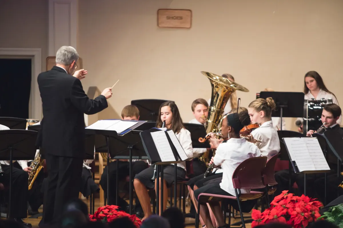 A conductor leading middle school band and strings students in concert