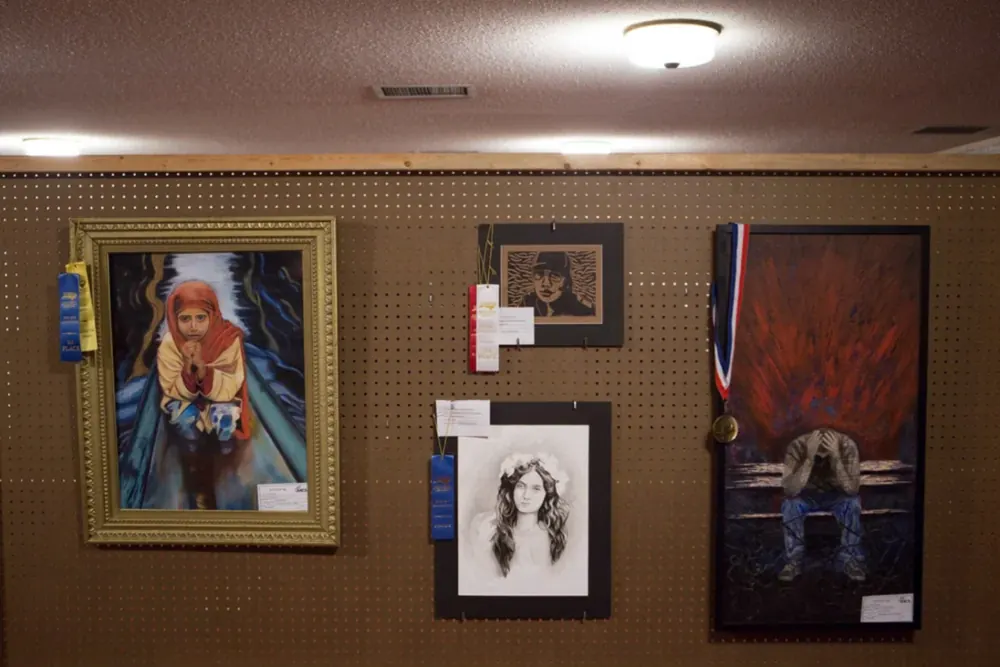 Award-winning student paintings and drawings on display with ribbons and a medal