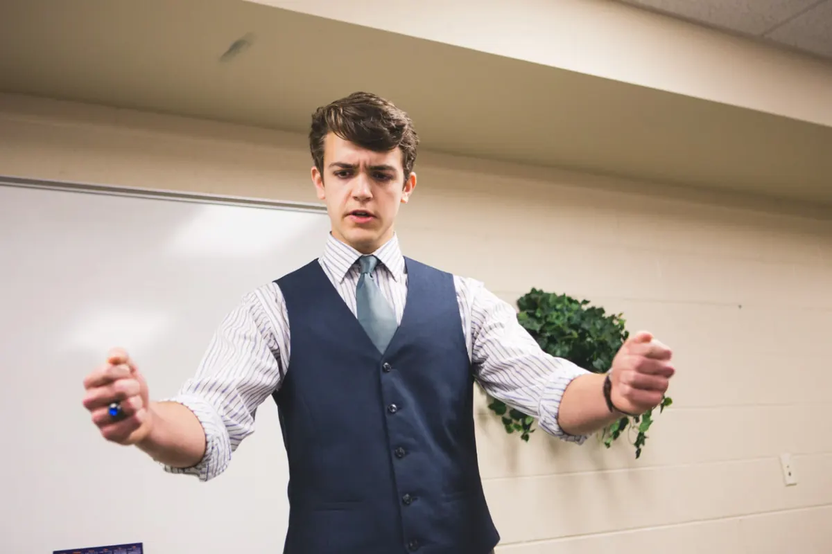 A high school student delivering a speech with expressive gestures