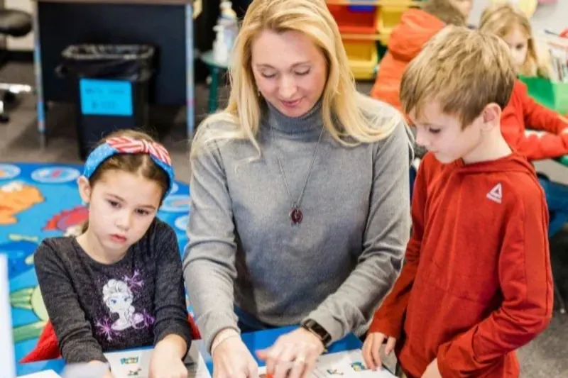 A teacher working alongside two elementary students at their table