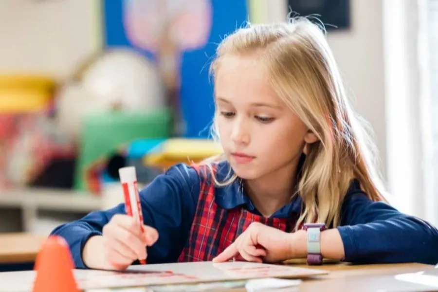 An elementary student in uniform writing carefully at her desk