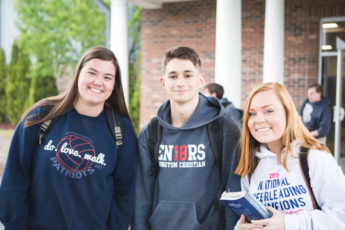 Three smiling seniors in WCA sweatshirts outside a campus building