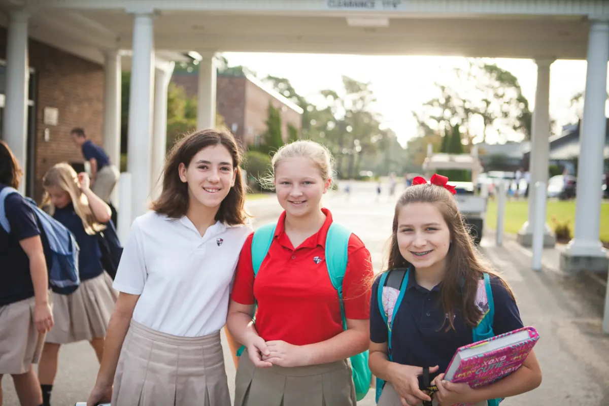 Three middle school girls in uniform smiling outside a campus building