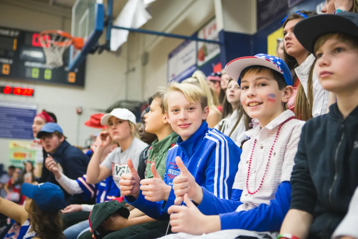 Middle school students cheering from the gym bleachers with thumbs up