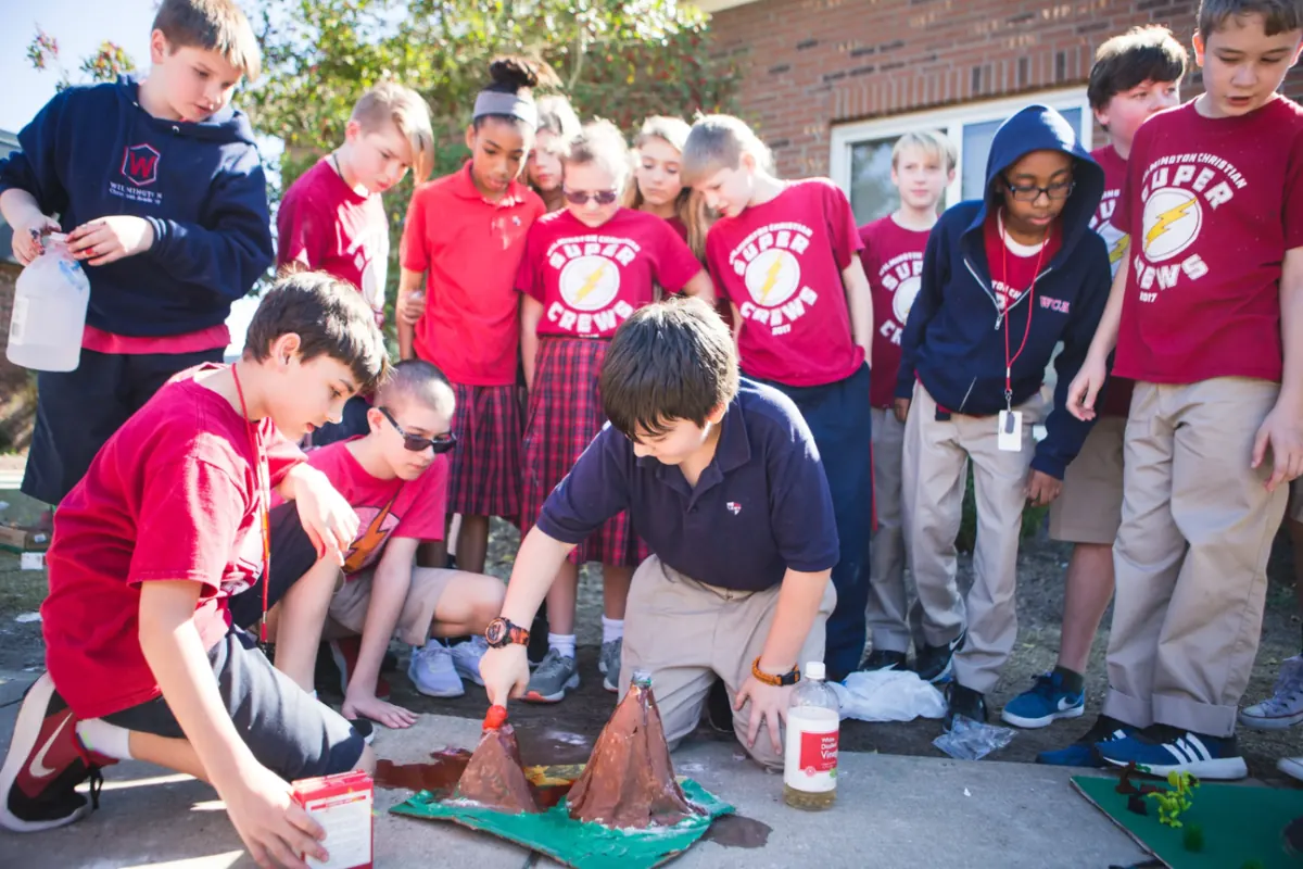 Students in crew shirts gathered around a baking soda volcano experiment