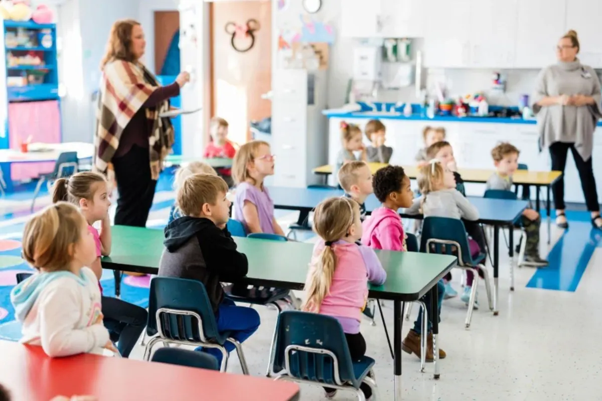 Preschoolers seated at classroom tables during a lesson with their teachers