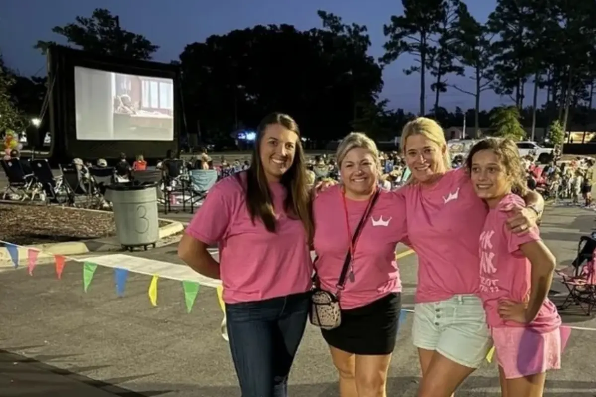 Four PTF members in pink shirts at an outdoor movie night on campus, with families watching a big screen behind them