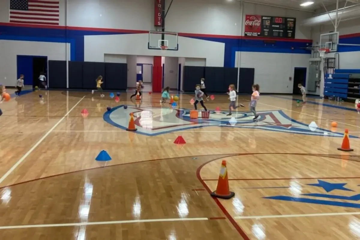 Young campers running a cone and ball course across the WCA gym floor