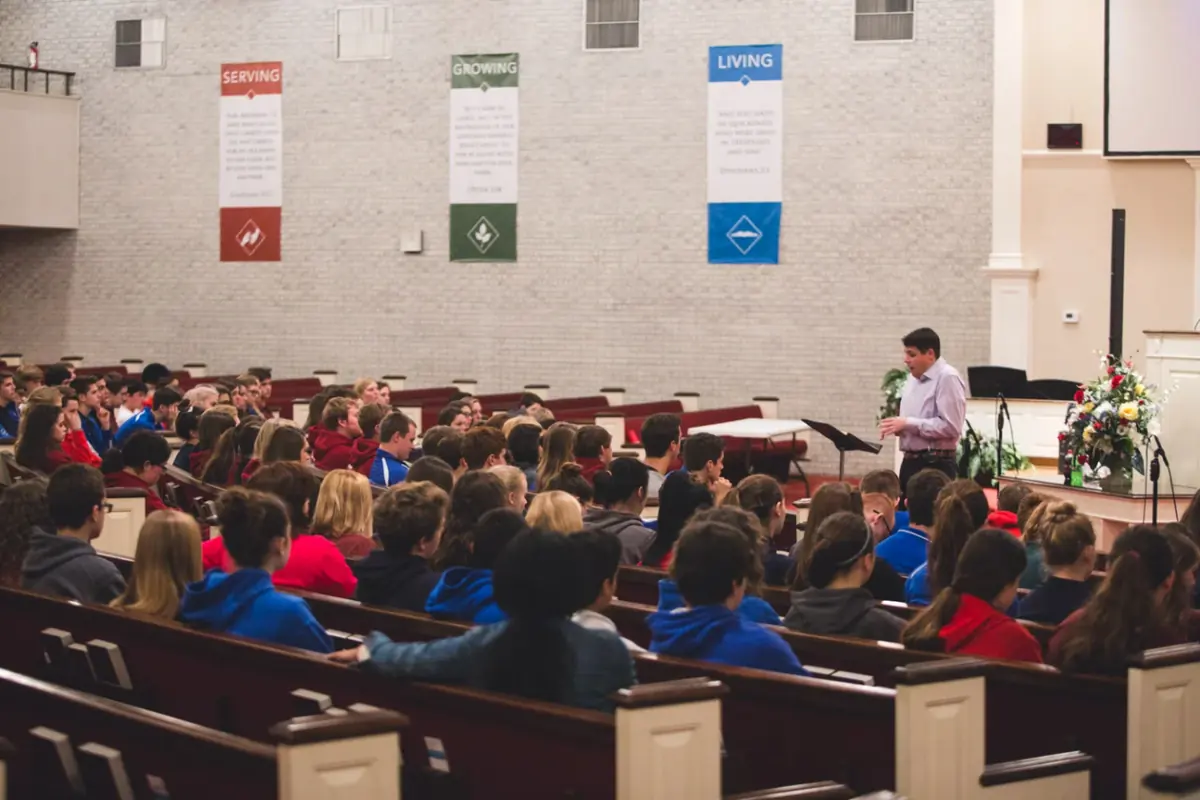 High school students in chapel in the Grace Baptist Church sanctuary, listening to a speaker beneath Serving, Growing, and Living banners