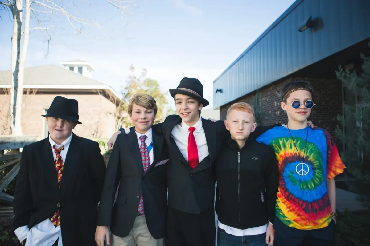 Five middle school boys in dress-up day outfits: suits, fedoras, a red tie, and a tie-dye shirt with a peace sign