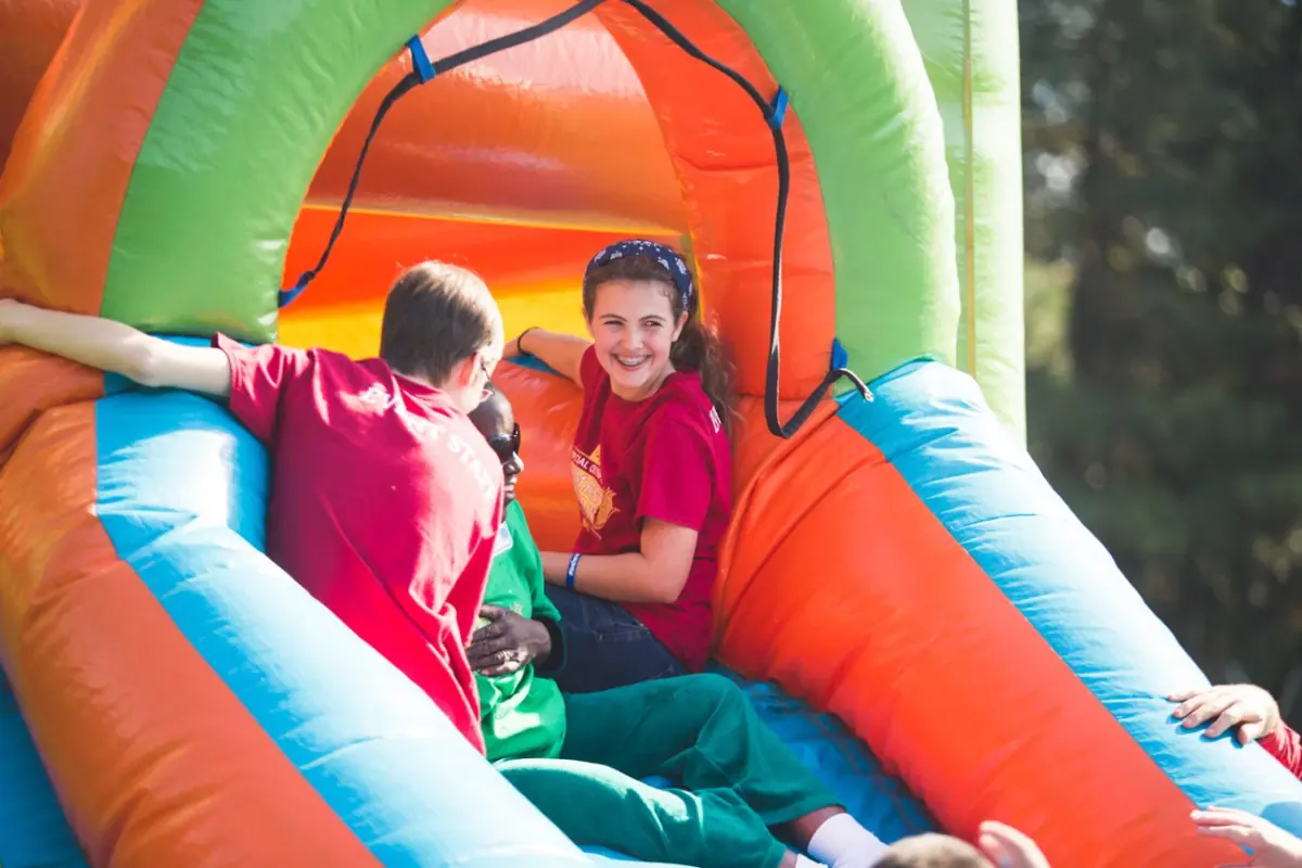 WCA student volunteers in Special Olympics event staff shirts sharing an inflatable slide with a participant